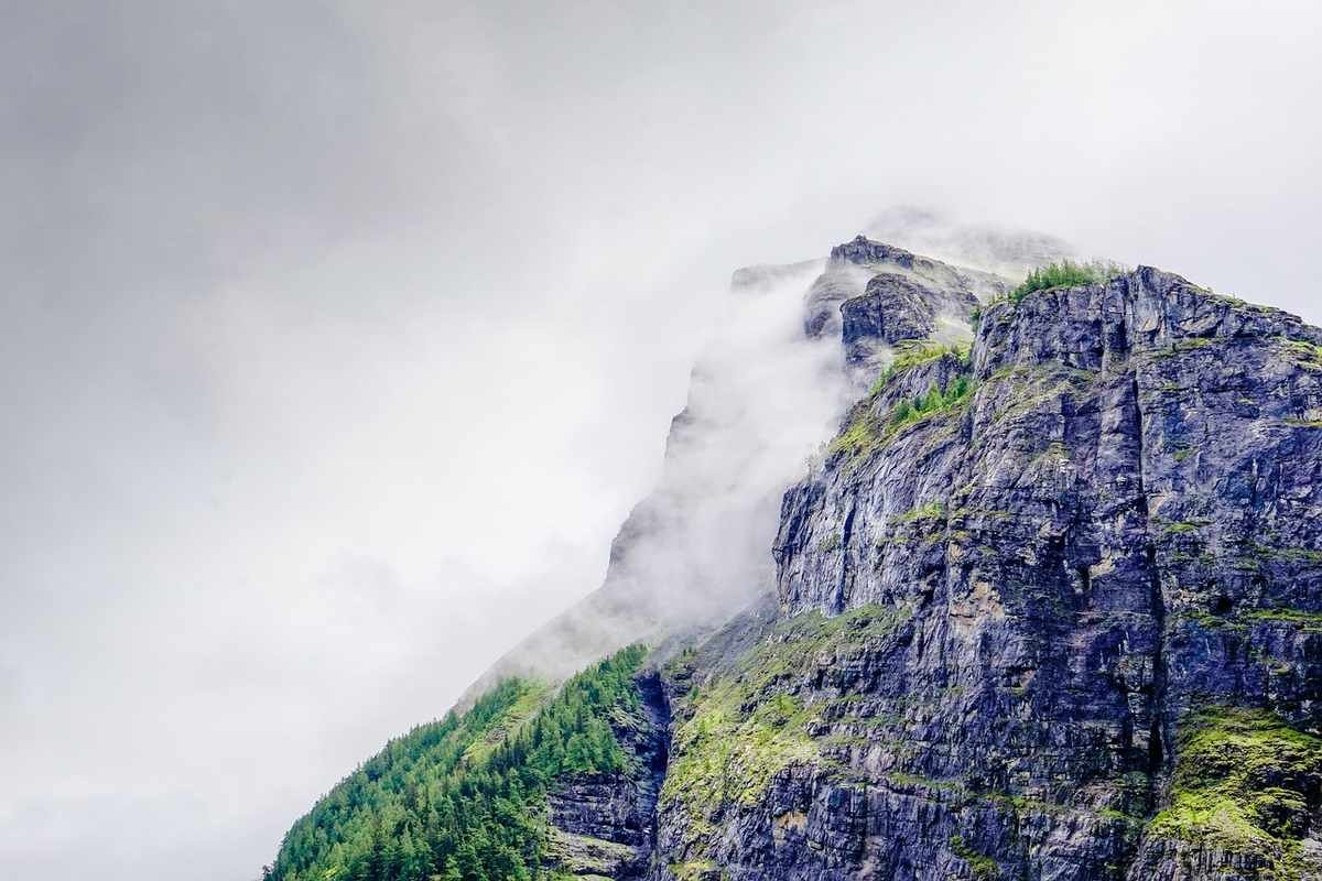 Falaise rocheuse escarpée enveloppée de brouillard avec végétation verdoyante sur les flancs