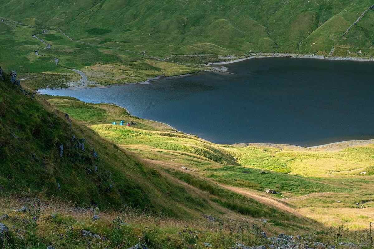 Lac alpin aux eaux bleues entouré de pentes herbeuses et de montagnes boisées